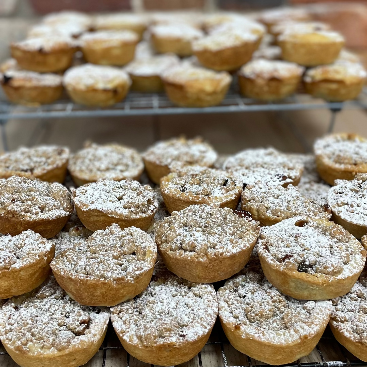 Home made mince pies dusted with icing on a cooling rack with a brick wall background