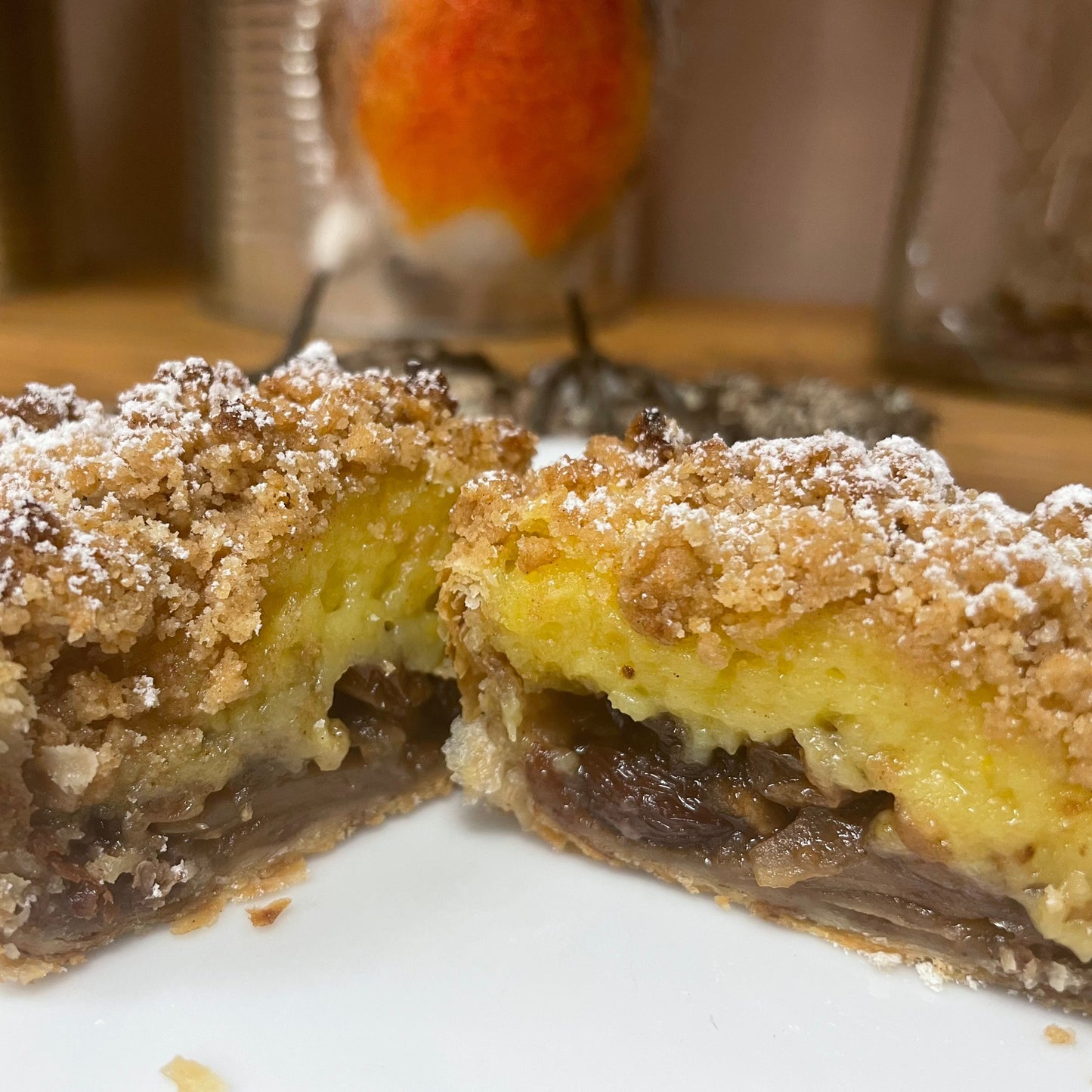 Mince pie cut in half filled with custard with a crumbly topping on a white plate with a blurred background