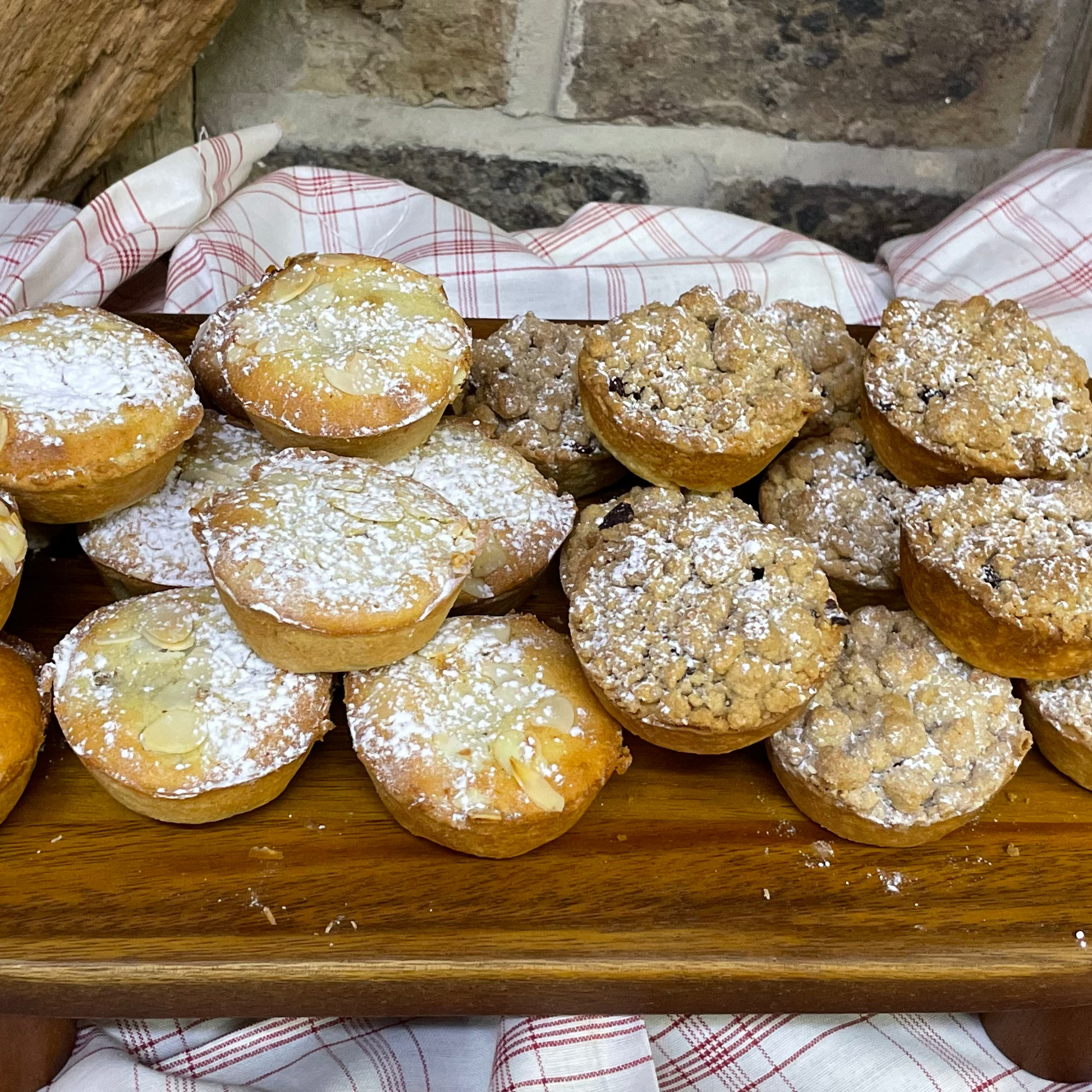 Wooden platter with assorted mince pies dusted in icing sugar on a checkered cloth